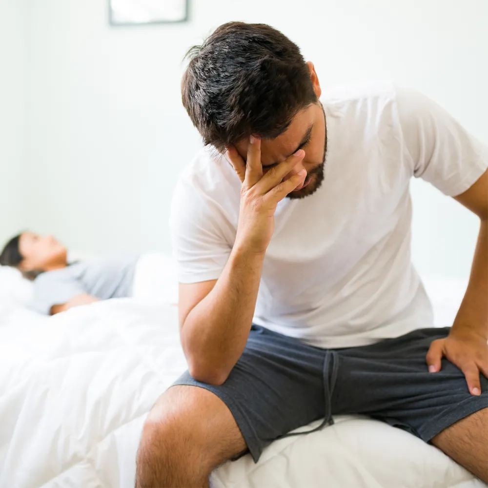 Distressed man seated on a bed beside his partner