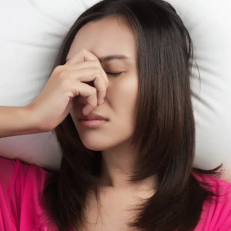 A woman resting her fingers against the bridge of her nose with a headache, one of the everyday symptoms a complete blood count helps explain