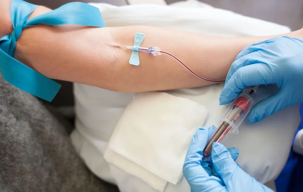 Gloved clinician collecting a venous blood sample into a vacuum tube from a patient's arm for a CRP (C-reactive protein) test