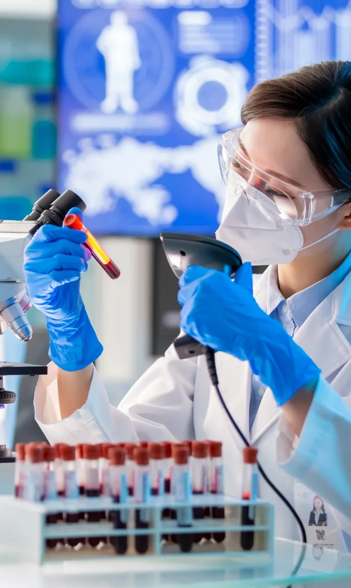 A laboratory scientist in a mask and goggles examining a blood sample tube during accredited analysis in Dubai