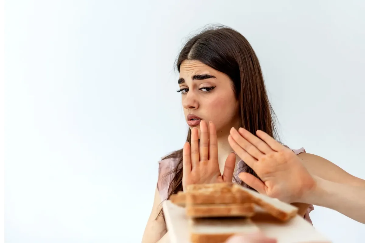 A woman at a table pushing away a plate of bread and pastries, illustrating the food intolerance test at home in Dubai.