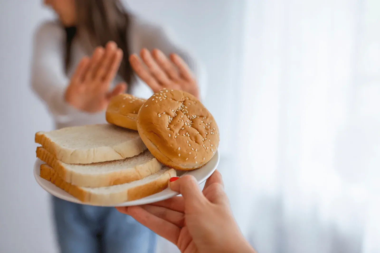 Woman raising both hands to decline a plate of sliced white bread and burger buns held out to her
