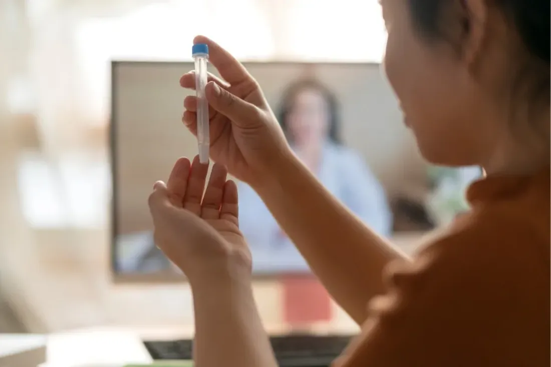 Woman at home holding a capped sample tube during a video consultation with a Vesta Care doctor about her hormone testing in Dubai