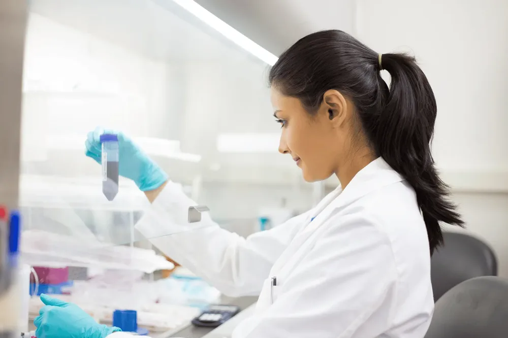 A laboratory scientist in a white coat handling a sealed sample tube inside a safety cabinet at the accredited Dubai laboratory that reports Vesta Care semen analyses