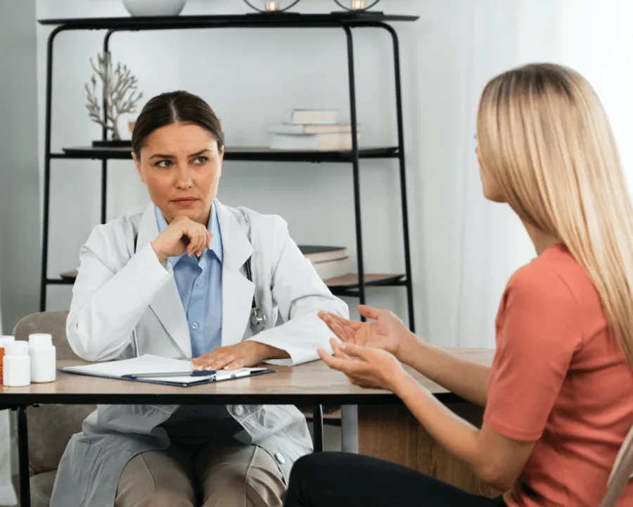 A DHA-licensed female doctor listening privately to a patient describing genital irritation and discharge, the consultation that leads to a confidential Trichomoniasis test at home in Dubai