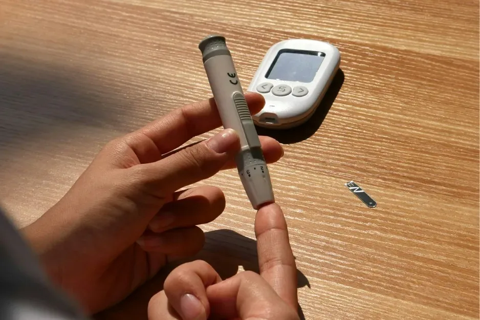 Person performing a finger-prick test beside a glucose meter