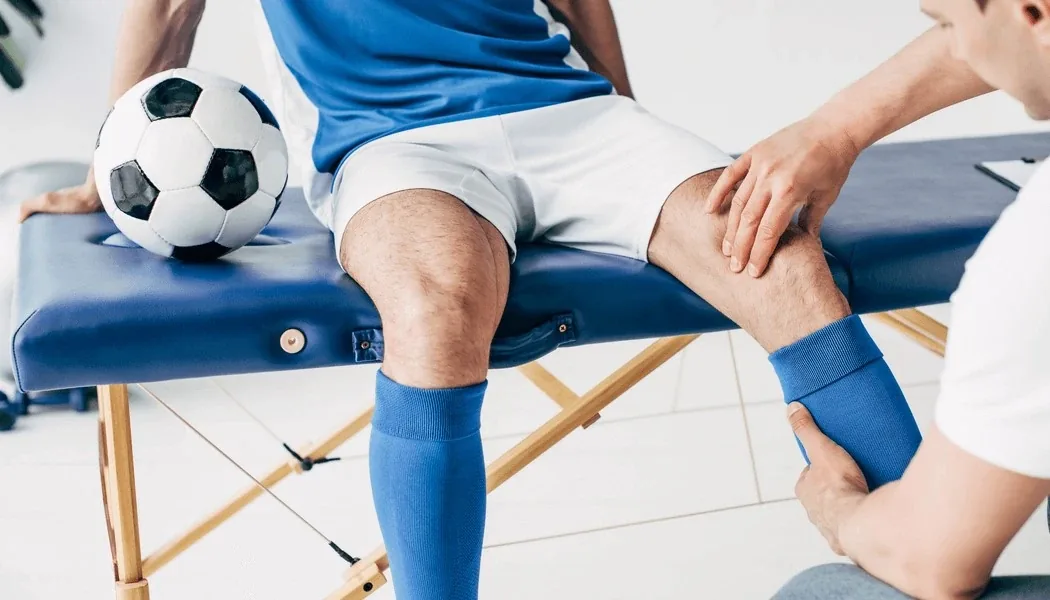 Physiotherapist supporting an injured football player's knee