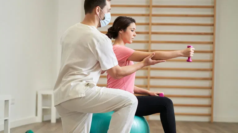 Physiotherapists guiding a woman through seated rehabilitation exercises