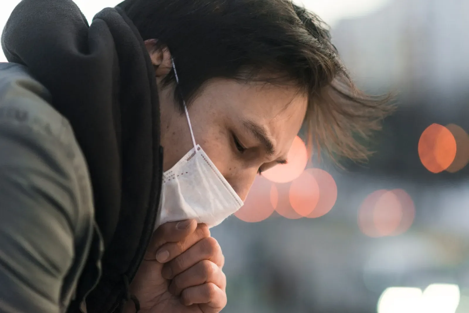 Ill man coughing into his sleeve outdoors